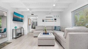 Una sala de estar moderna con un sofá seccional gris, una mesa de centro con un jarrón, un televisor de pantalla plana y una exhibición de tabla de remo de paddleboard montada en la pared.