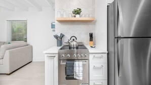 Una cocina moderna con estufa, horno y refrigerador de acero inoxidable, un estante de madera con cristalería, y una planta.