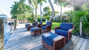 A wooden deck with wicker furniture and a view of the water and palm trees. - The Riverside Retreat #2 (Fort Lauderdale)