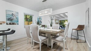 A modern dining area with a wooden table and white chairs, a hanging light fixture, and artwork on the walls. - The Riverside Retreat #2 (Fort Lauderdale)