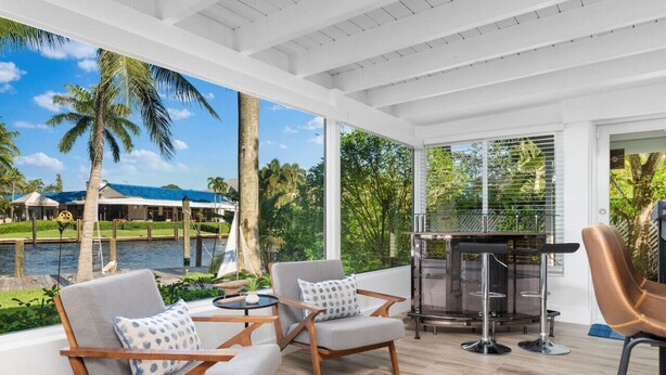 A spacious outdoor area with a pool, two chairs, a table, and a bar area with stools. - The Riverside Retreat #2 (Fort Lauderdale)