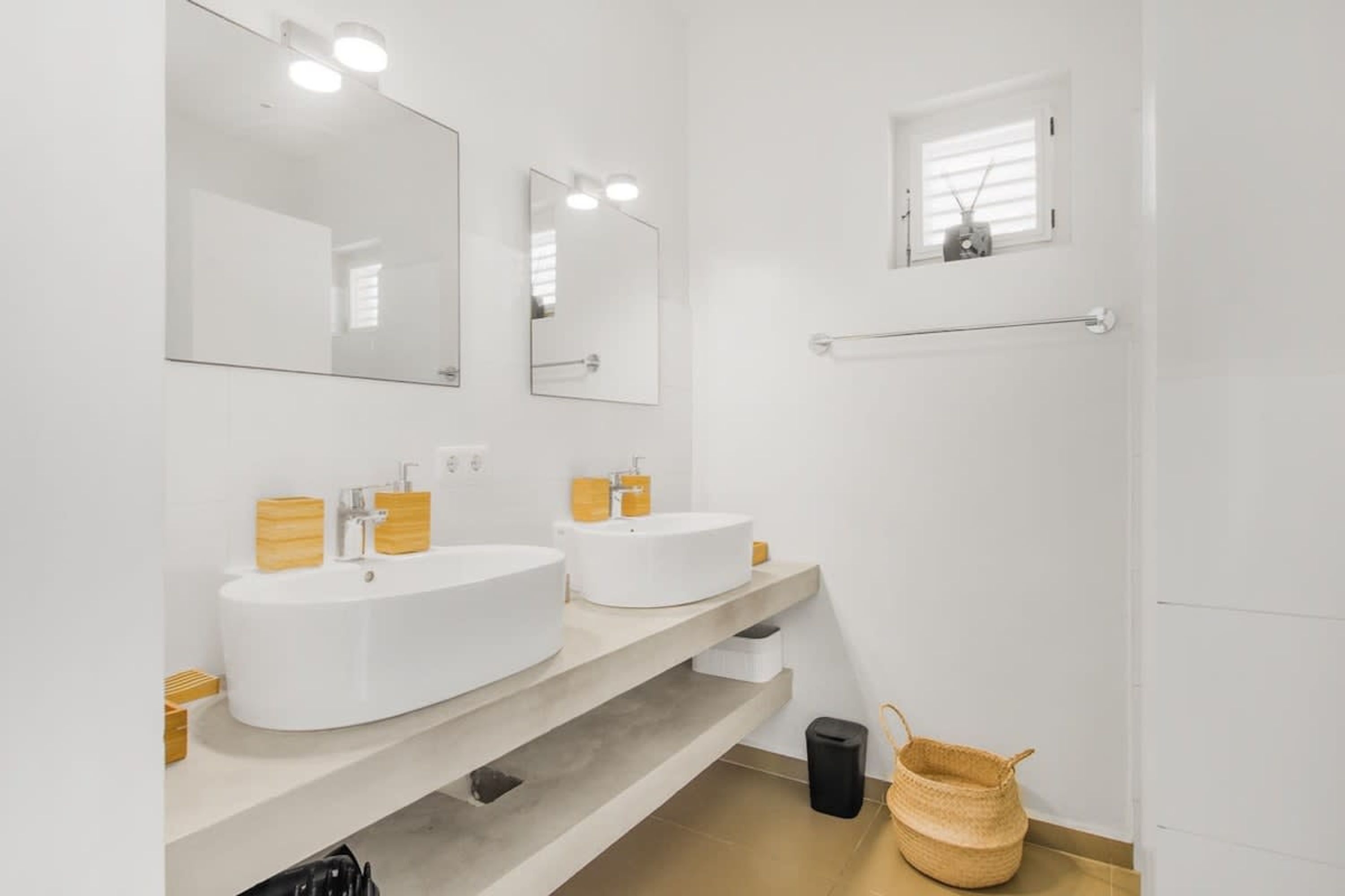Un baño moderno con dos lavamanos, un espejo grande y una ventana pequeña.