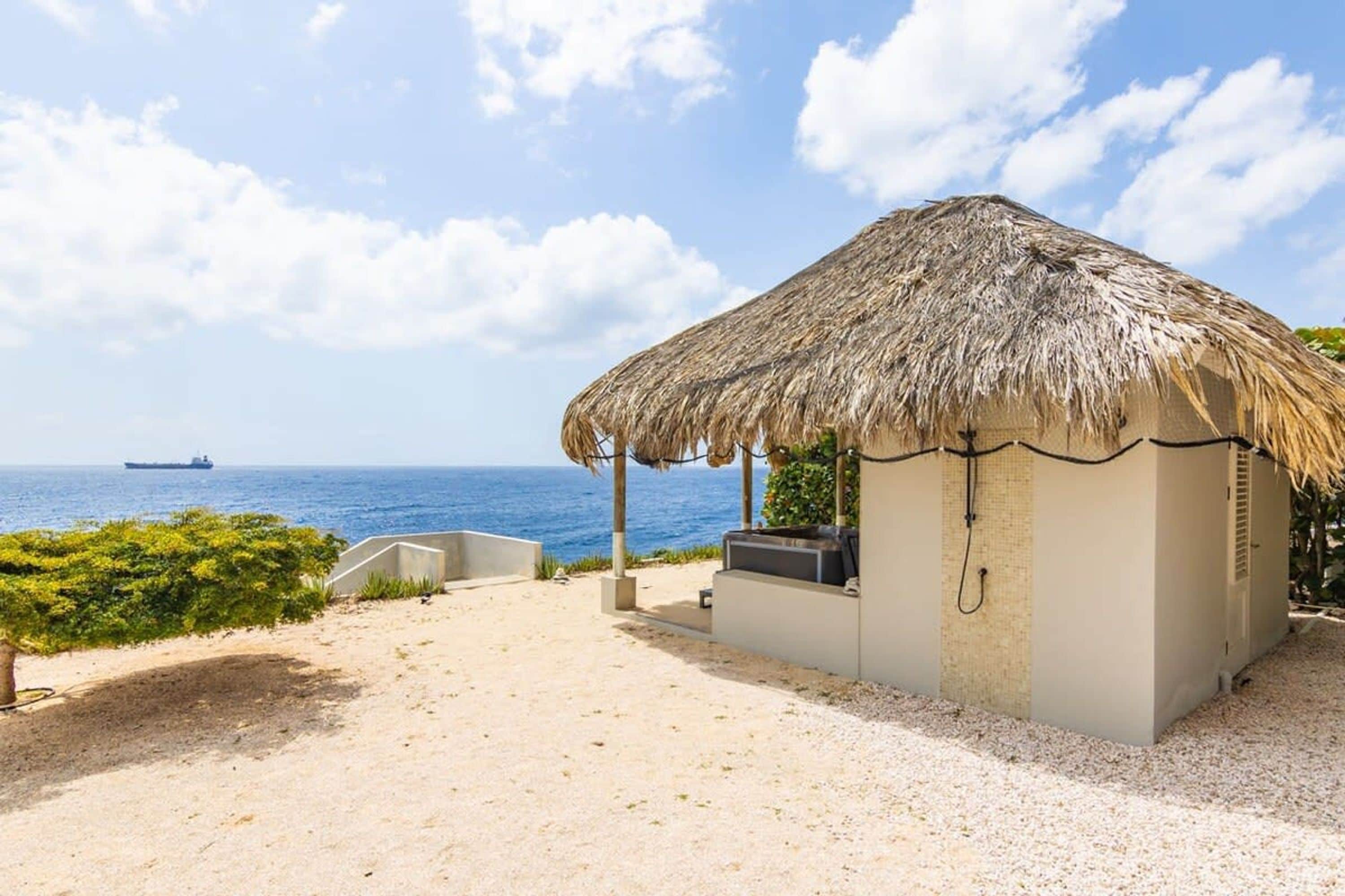 Eine Strandhütte mit einem Reetdach, einem Grill und einer Sitzecke mit Blick aufs Meer.
