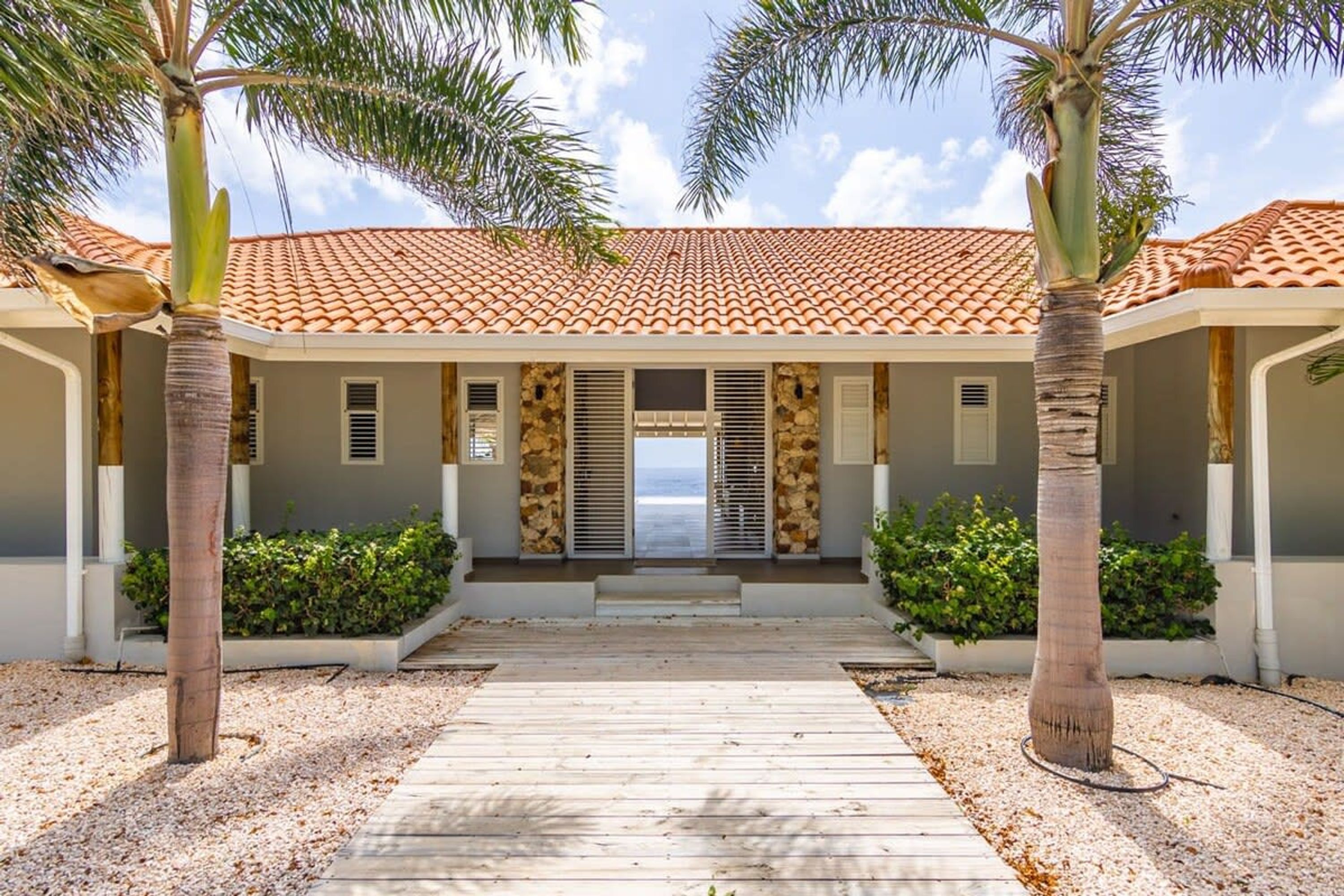 A resort with a tiled roof, palm trees, and a wooden walkway leading to the entrance.