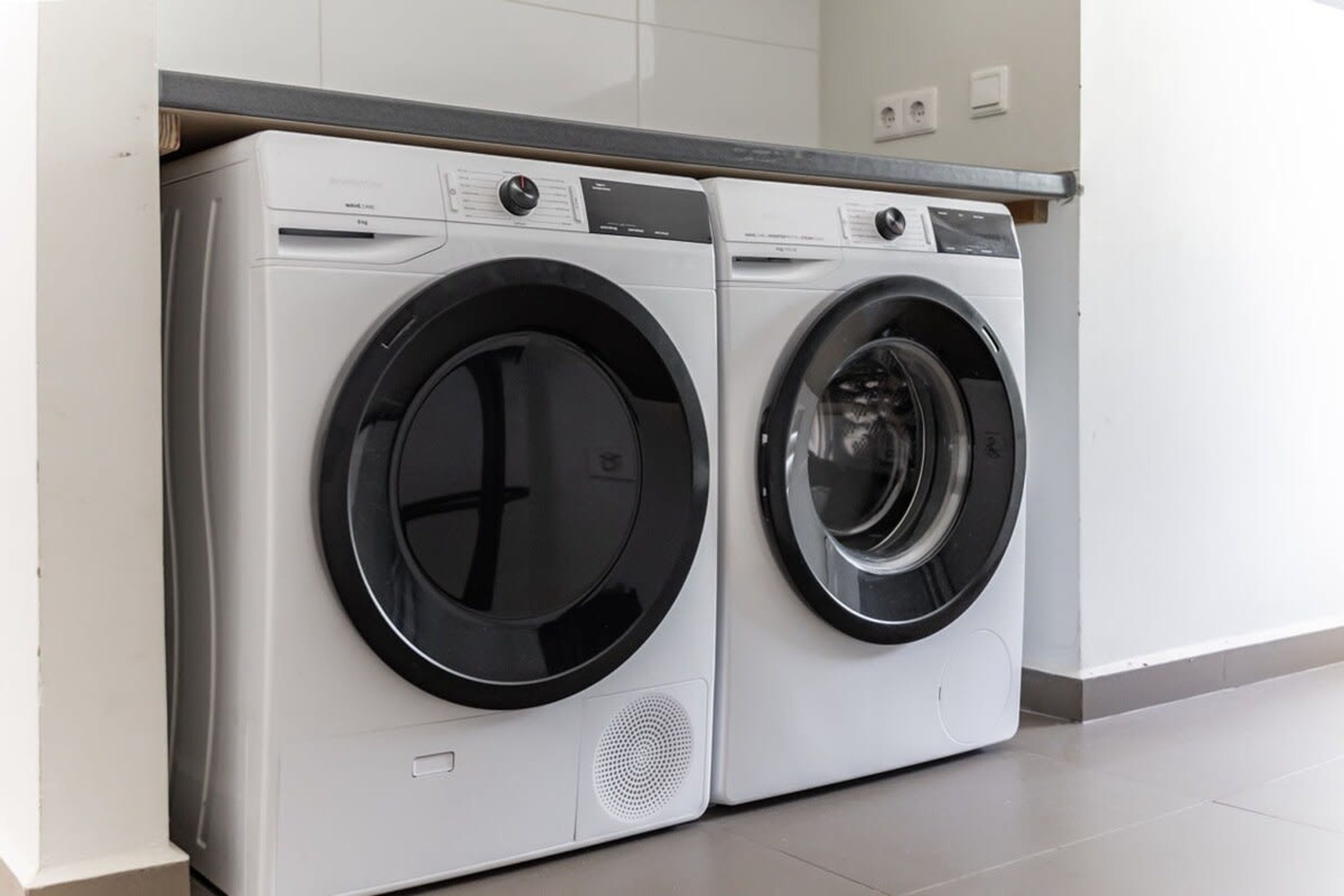 A pair of front-loading washing machines in a modern kitchen with white cabinets and a grey countertop.