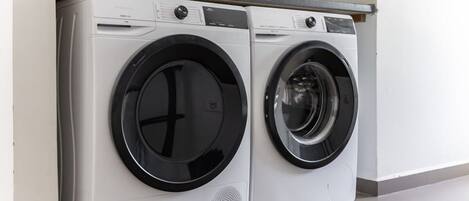 A pair of front-loading washing machines in a modern kitchen with white cabinets and a grey countertop.