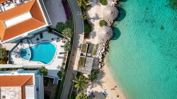 An aerial view of a resort with a swimming pool, beach, and clear turquoise waters.