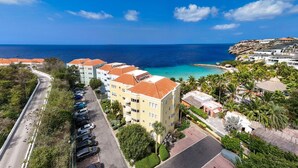 A coastal hotel with multiple buildings, a parking lot, and a view of the ocean. - Serenity by the Seascape Marble Blue Bay Bliss (Sint Michiel)