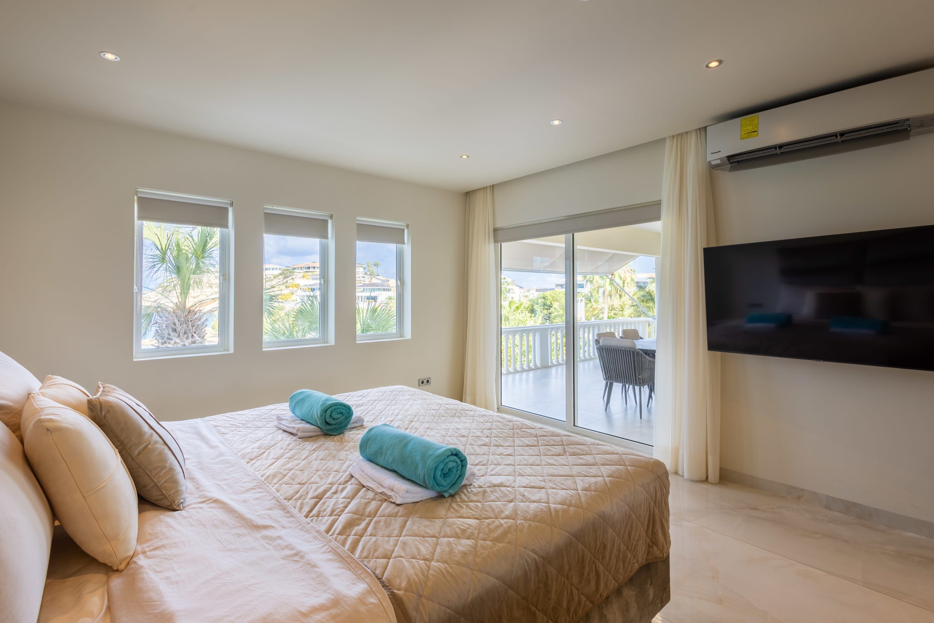 A hotel room with a large bed, two windows, a balcony with a TV, and an air conditioning unit.