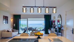 A modern kitchen with a central island, a dining area with chairs, and a view of the ocean. - Serenity by the Seascape Marble Blue Bay Bliss (Sint Michiel)