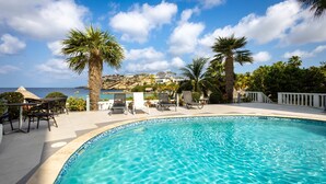 A swimming pool with lounge chairs, palm trees, and a view of a coastal area. - Serenity by the Seascape Marble Blue Bay Bliss (Sint Michiel)