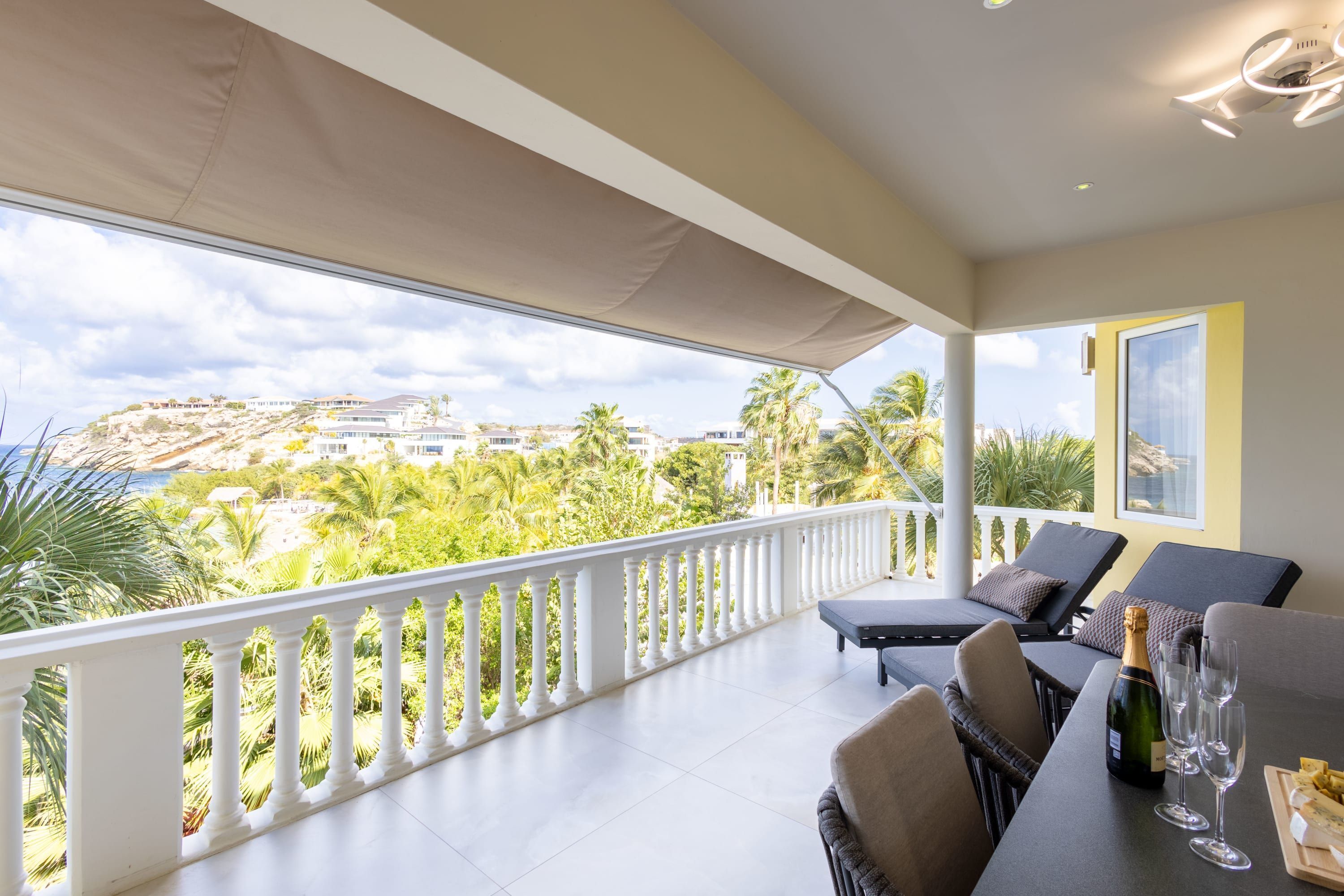 Un balcon doté d’une balustrade blanche, d’un espace salon extérieur et d’une table sur laquelle se trouvent une bouteille et des verres.