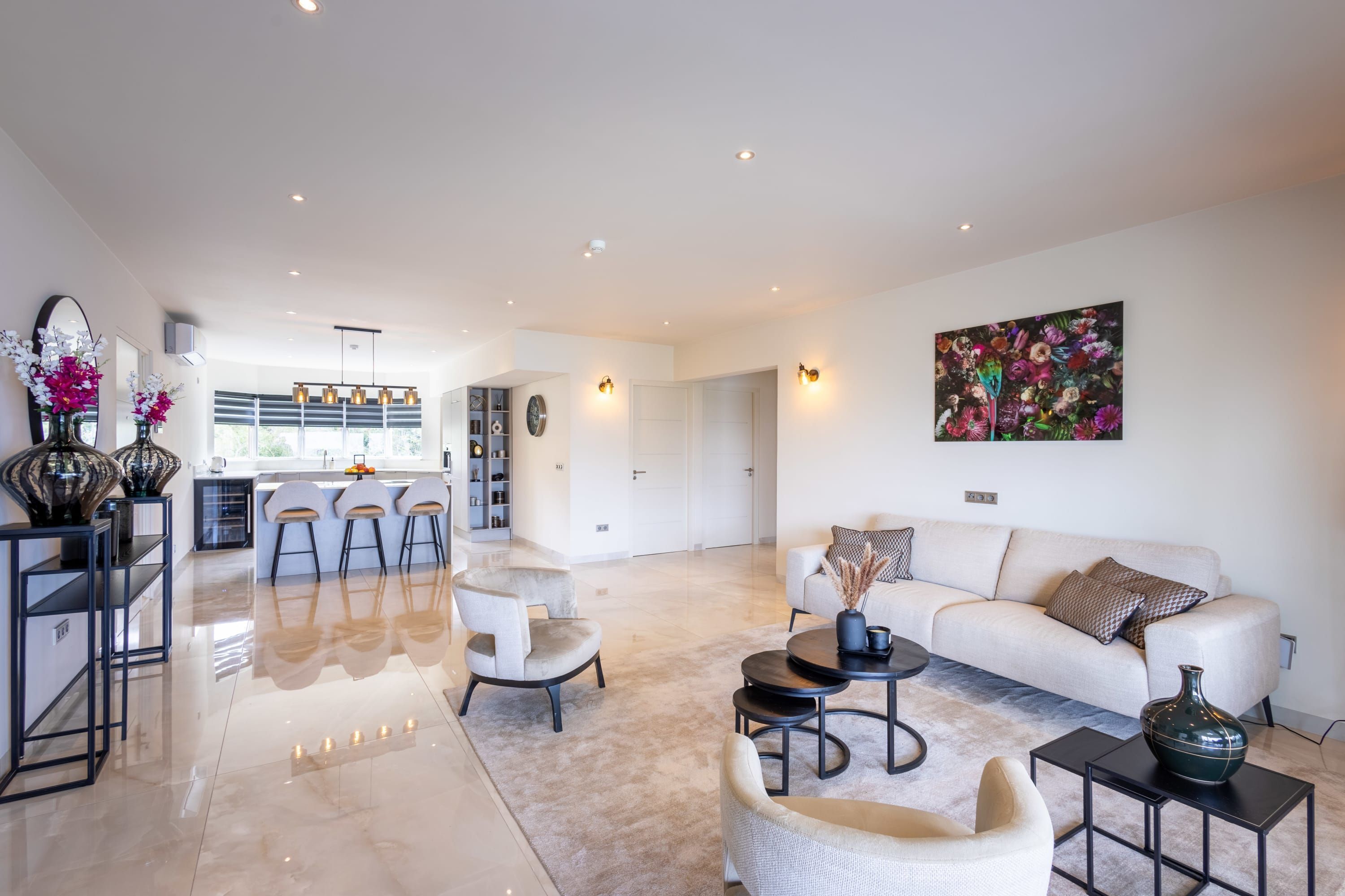 A spacious living area with a sofa, chairs, a coffee table, and a kitchen in the background.