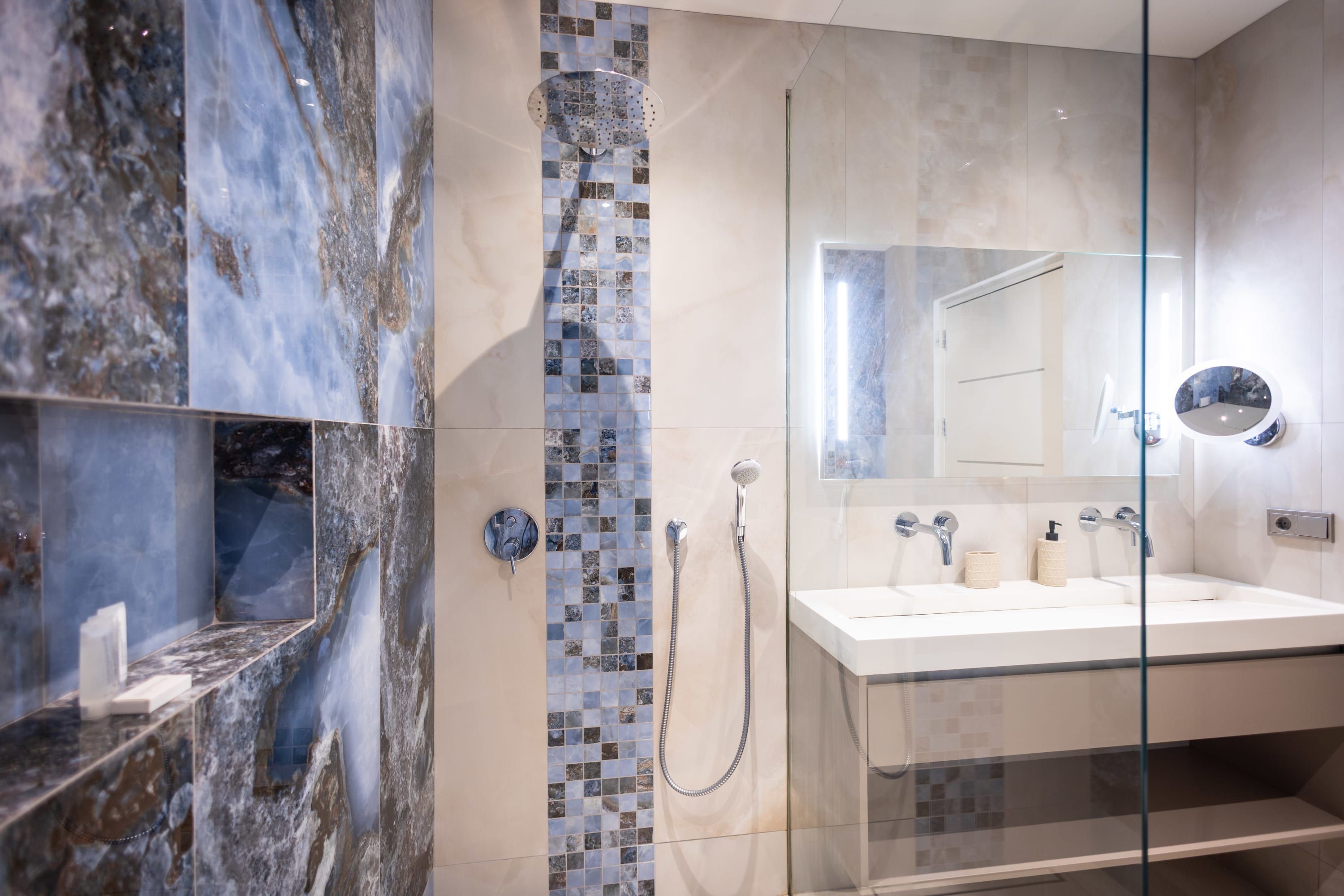 A modern bathroom with a glass shower enclosure, a marble vanity, and a large mirror.