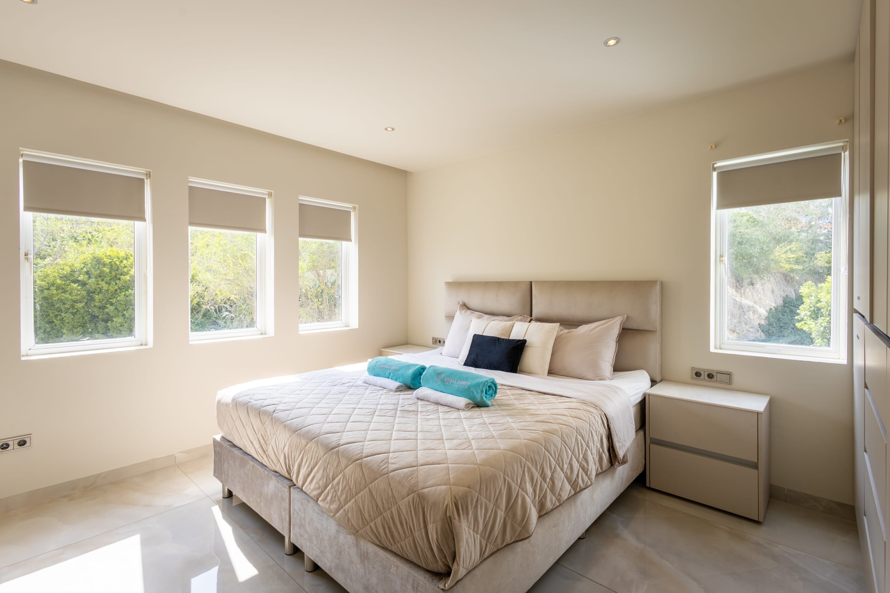 Une chambre à coucher avec un grand lit, deux tables de chevet et trois fenêtres.