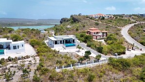 Una proprietà costiera con diversi edifici, tra cui una casa moderna con piscina, una costruzione più piccola e un edificio più grande con tetto rosso.