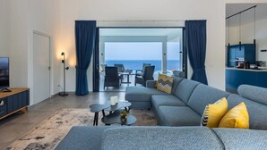 Un soggiorno moderno con un divano grigio, un tavolino da caffè e vista mare attraverso una porta in vetro.