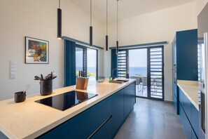 Eine moderne Küche mit einer großen Kochinsel, Pendelleuchten und Blick ins Freie.