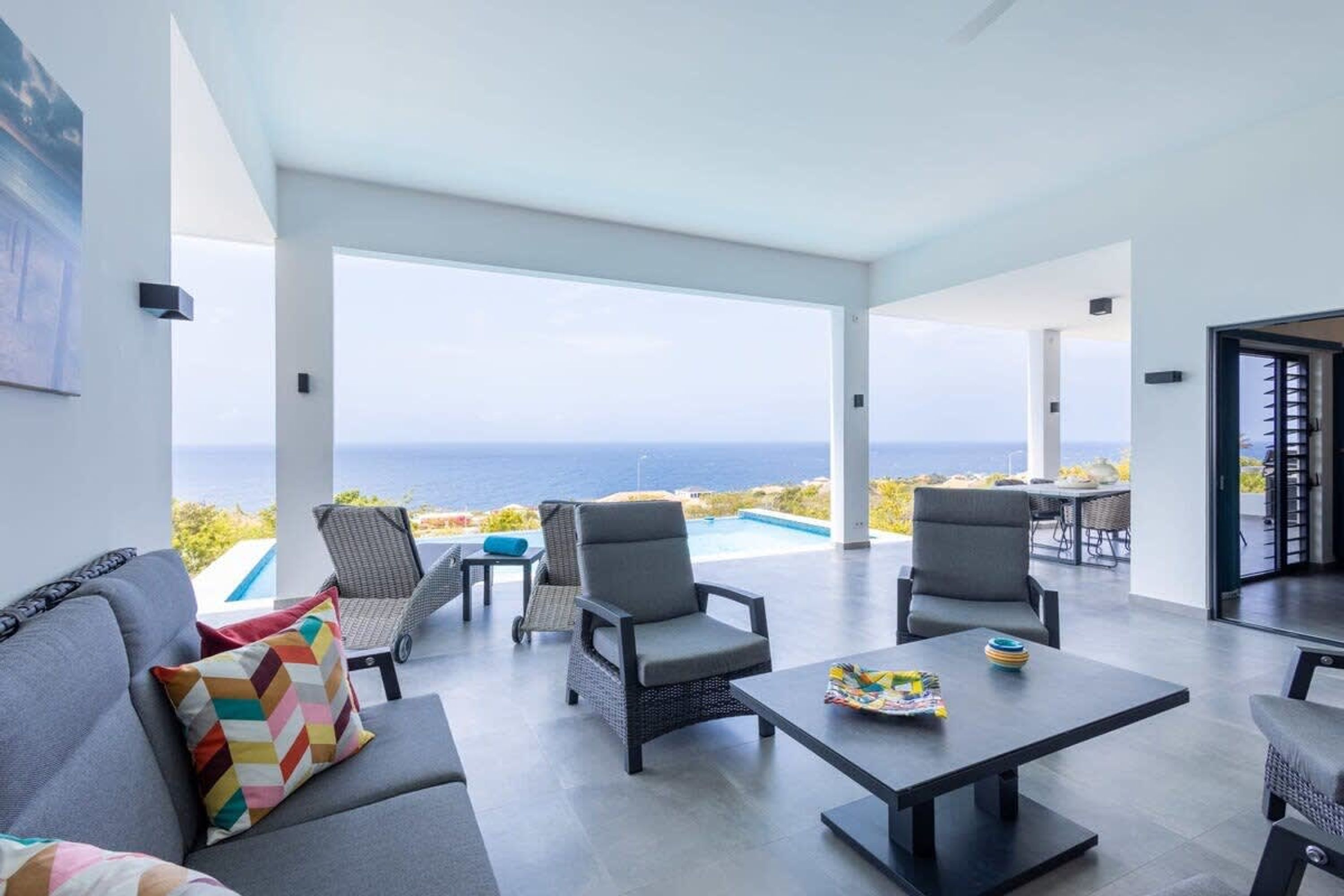 A modern living room with a view of the ocean, furnished with sofas, chairs, and a table.