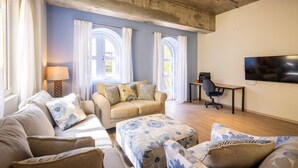 Una sala de estar con un sofá, un reposapiés y un televisor en la pared.