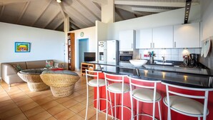 Ett modernt kök med en central köksö, vita skåp och en röd accentvägg. Runt köksön står tre vita barstolar.