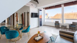 Un soggiorno moderno con tavolo da pranzo in vetro, sedie blu, un divano e una TV fissata alla parete.