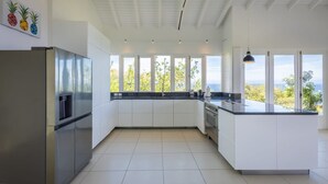 Una cocina moderna con armarios blancos, electrodomésticos de acero inoxidable y grandes ventanales con vistas al exterior.
