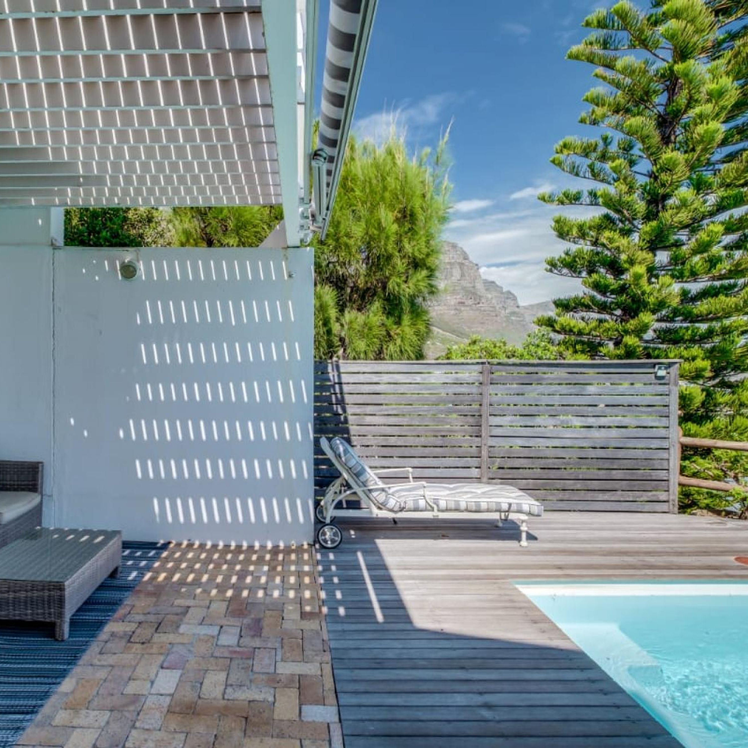 Zona de piscina con una silla de descanso, una terraza de madera y vistas a una montaña.