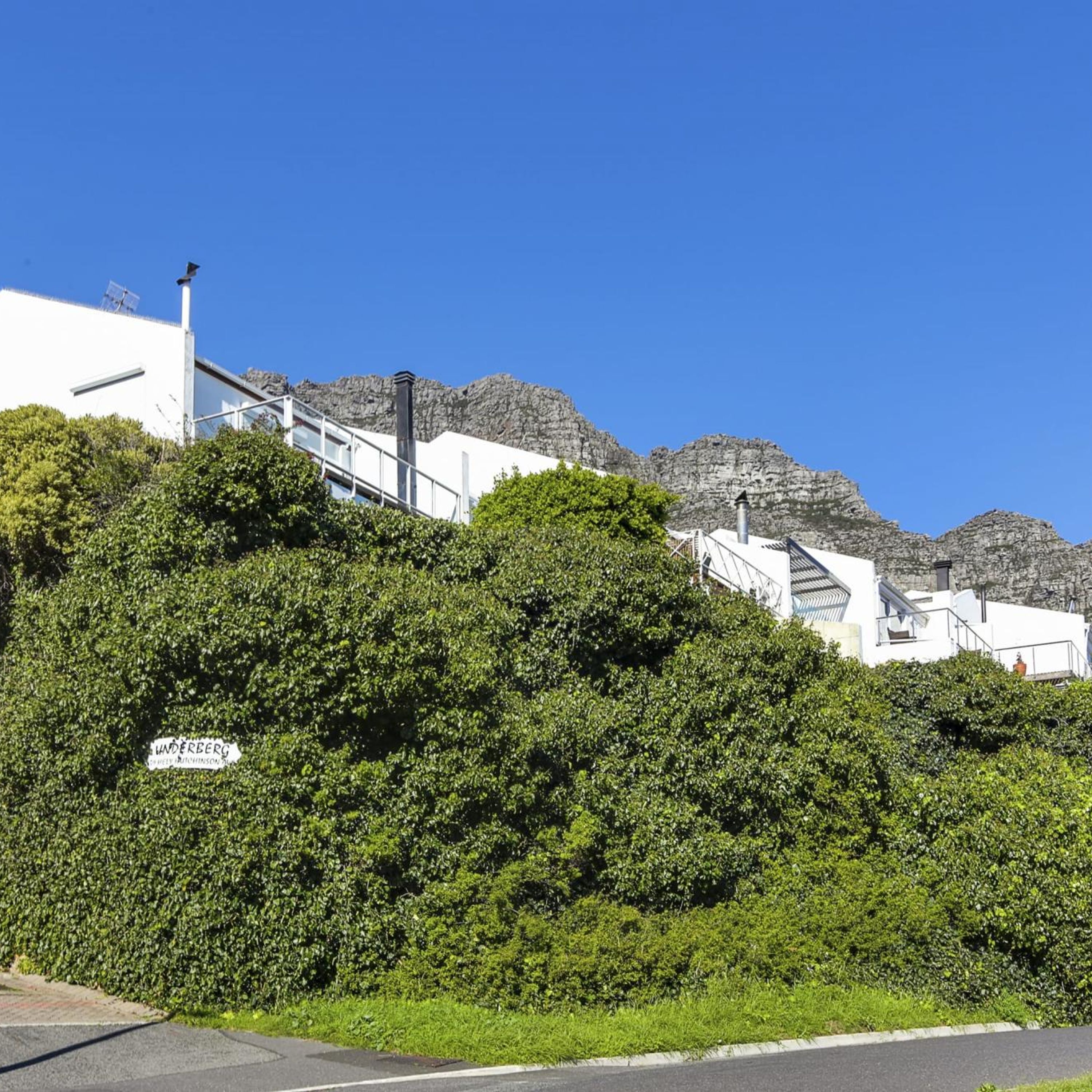 A white building with a sign reading "UNDERBERG" amidst lush greenery and rocky mountains in the background.