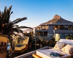 A modern hotel room with a large bed, a view of a mountain, and a pool area. - Stylish Penthouse w Private Pool and Parking Houghton Penthouse (Cape Town)