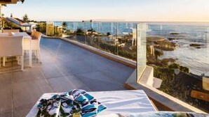 Een terras met uitzicht op de oceaan, met een tafel, een plaid en een stoel.