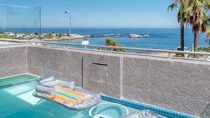 Ein Swimmingpool mit klarem, blauem Wasser, Blick auf den Ozean und eine Palme.