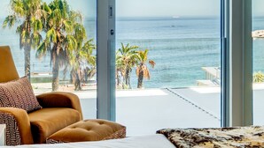 Ein Schlafzimmer mit großem Fenster und Blick auf Strand und Palmen.