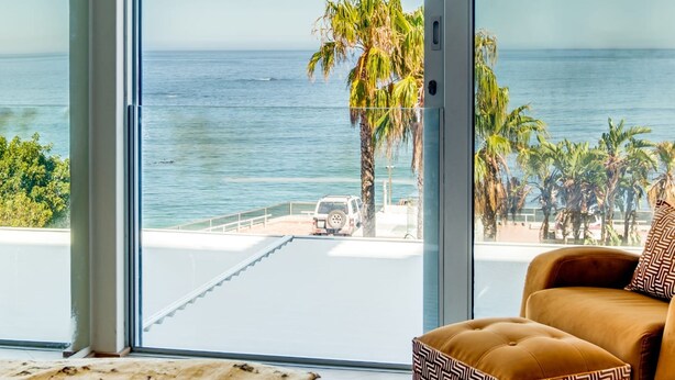 Ein Zimmer mit einer großen Schiebetür, die auf einen Balkon mit Blick auf das Meer und Palmen führt.