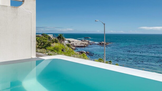 Une piscine à débordement moderne offrant une vue dégagée sur l’océan et le littoral rocheux.