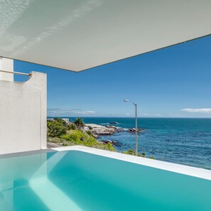 Una piscina infinita moderna con vista despejada al océano y a la costa rocosa.