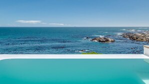 Une vue dégagée sur l’océan, avec une côte rocheuse et une piscine au premier plan.