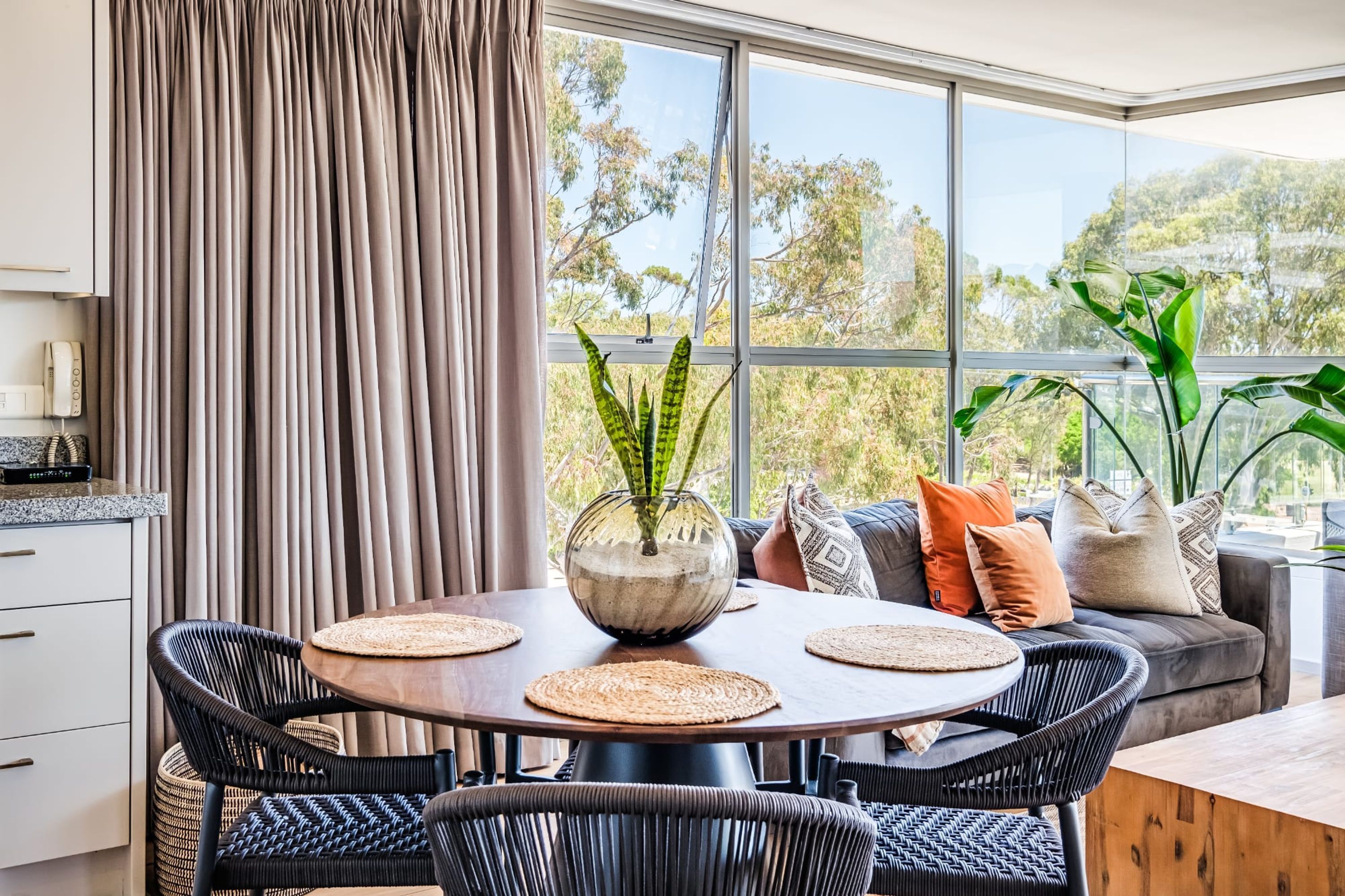A modern dining area with a round table, woven placemats, and a decorative vase.