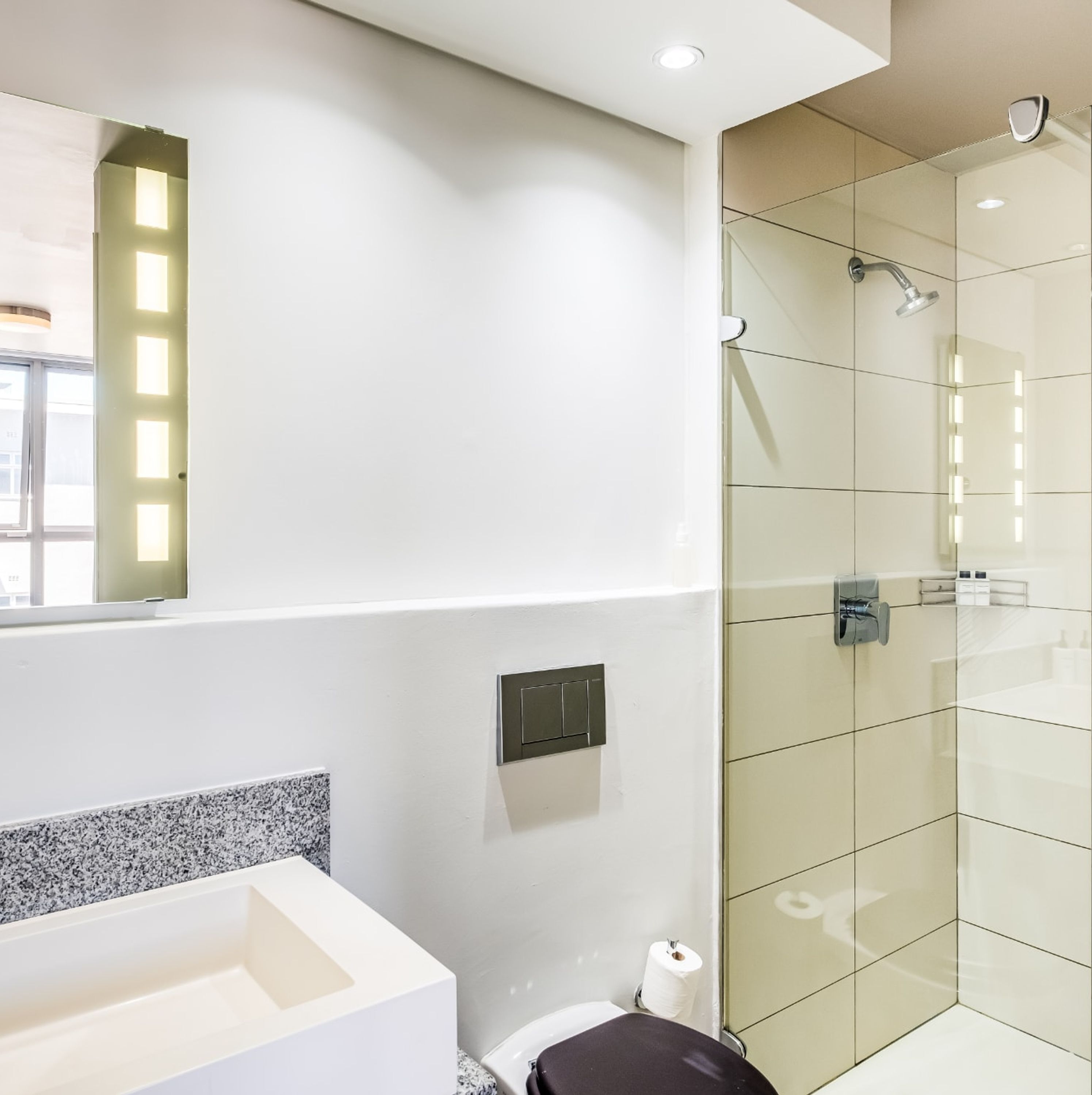 A modern bathroom with a large mirror, a shower with glass doors, and a toilet.