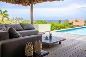 A wooden deck with a sofa and a table, overlooking a pool and the ocean. - Gosa Di Bida I Private Pool (St. Marie)