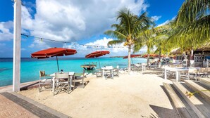 A beachside restaurant with outdoor seating, palm trees, and a view of the ocean. - Gosa Di Bida I Private Pool (St. Marie)