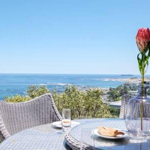 A table set for two with a clear view of the ocean and a cityscape in the background.