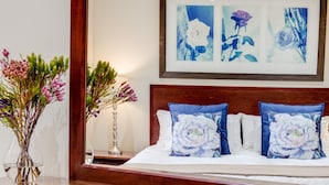 Una cama bien hecha con almohadas florales, un cabecero de madera y una mesita de noche con un florero.