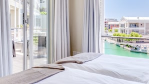 Habitación de hotel con cama, vista a un puerto deportivo y balcón con cortinas.