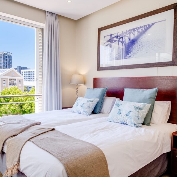 A hotel room with a large bed, a view of buildings, and a framed picture on the wall.