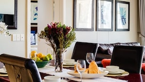 Un comedor con una mesa de madera dispuesta para dos personas, un jarrón con flores y cuadros en la pared.