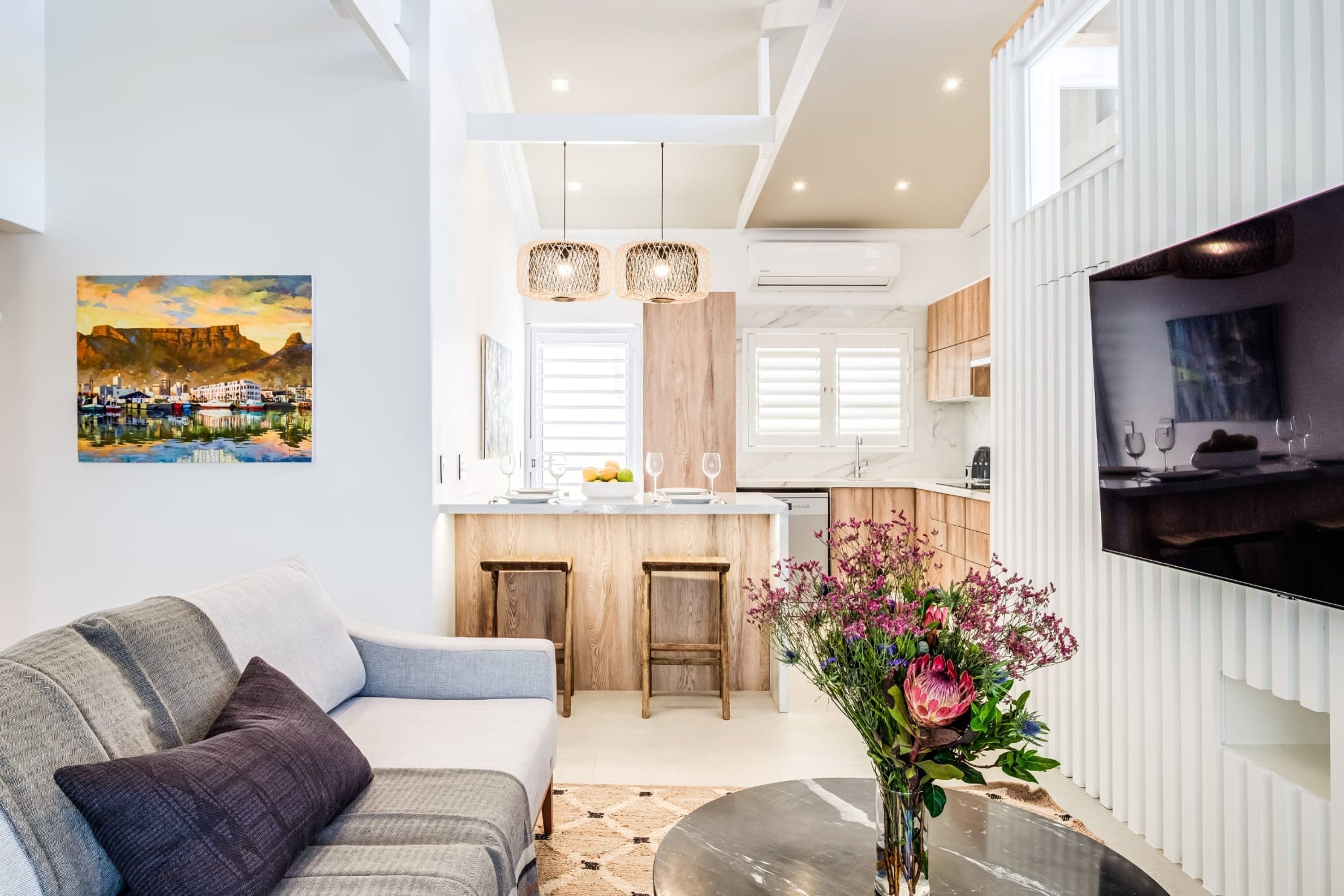 A modern living room with a sofa, a coffee table, and a painting of a coastal scene.