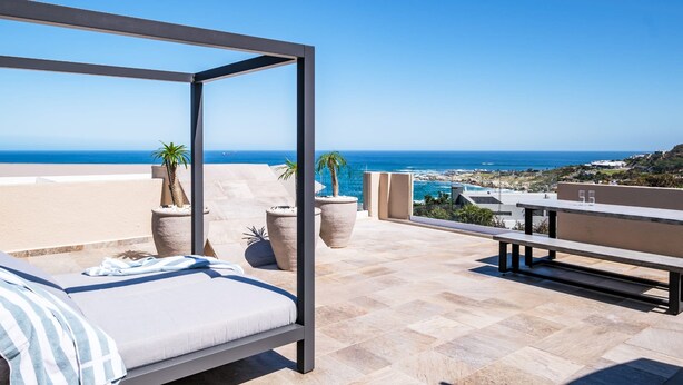 Un balcón con cama, plantas en macetas y vista al mar.