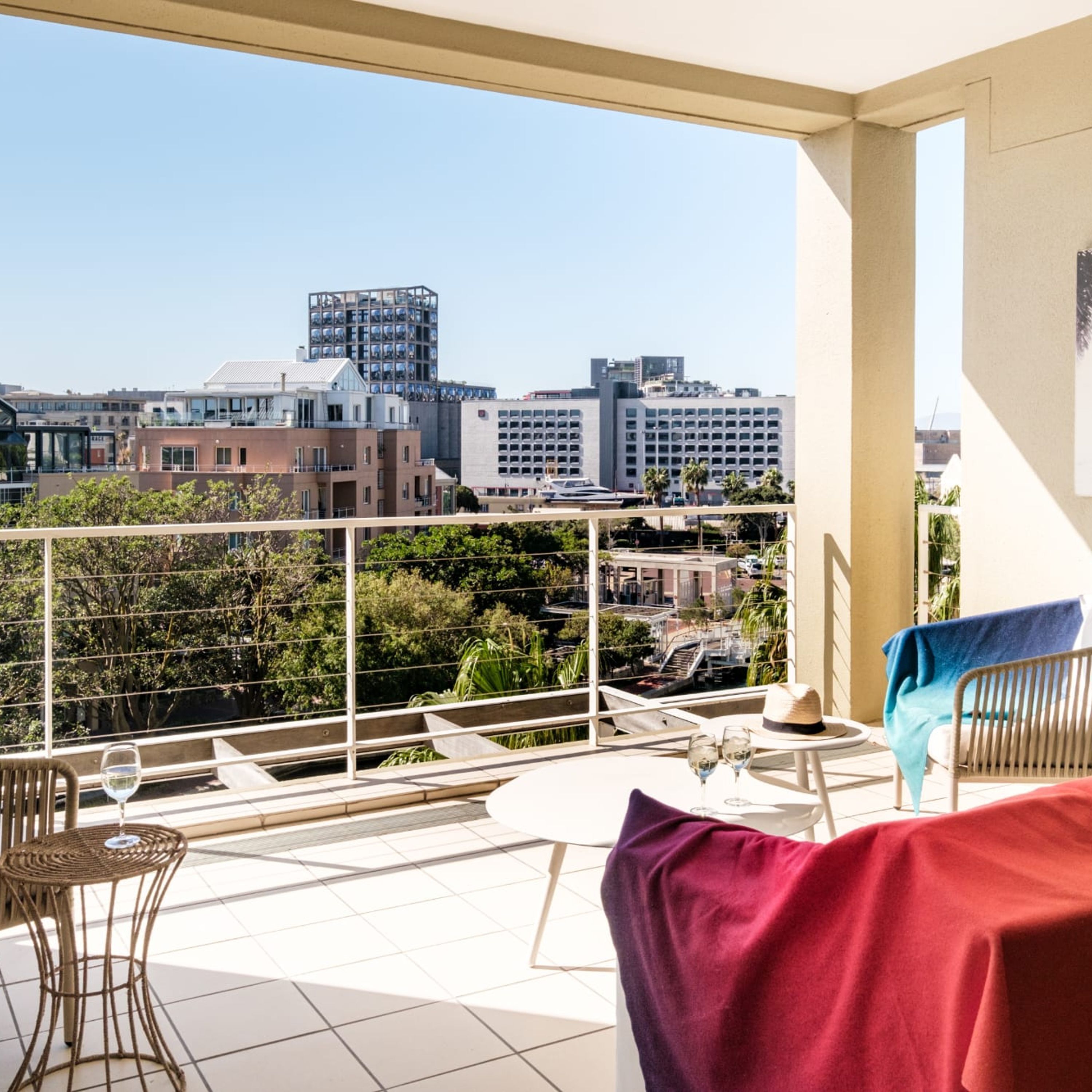 A balcony with a view of city buildings, a table with chairs, and a red cushion.