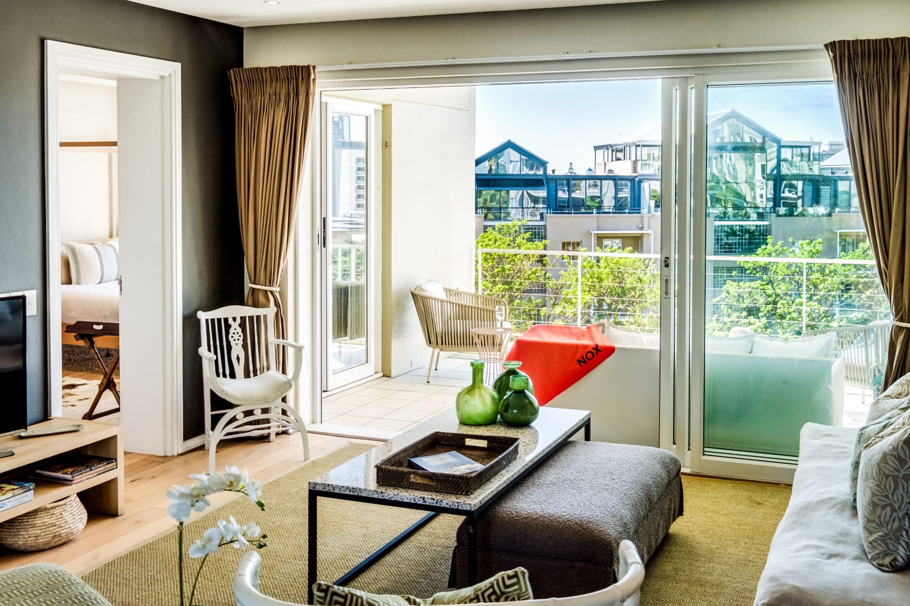 Una sala de estar moderna con sofá, una mesa de centro y televisor. Cuenta con un balcón que ofrece vistas a edificios y zonas verdes.
